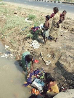 Poverty-stricken Women washing their clothes by a Road in Mumbai, India.