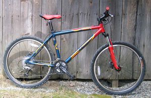 This mountain bicycle features oversized tires, a sturdy frame, front shock absorbers, and handlebars oriented perpendicular to the bike's axis