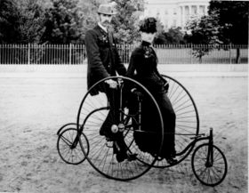 A smartly dressed couple seated on an 1886 "quadricycle" for two