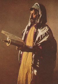 A Yemeni Jew wearing a kippah skullcap prays with a tallit shawl. The prayer box strapped to his forehead and arm are tefillin. His uncut side-curls are payot.