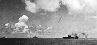 A Japanese Val dive bomber (center) is shot down during the attack on the Enterprise (lower right).  Enterprise is smoking from earlier bomb hits as another bomb near-misses the carrier.