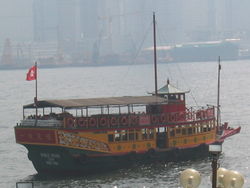 A tourist boat, with a HKSAR flag hanging on it, running on the Victoria Harbour on a misty day.