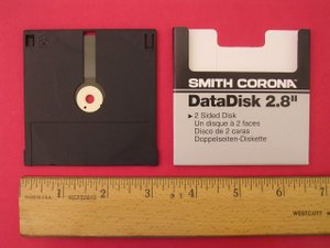 A Smith Corona DataDisk 2.8-inch actually measures about 3 1/32-inch square.  This disk is one of the few different Mitsumi Quick Disk packages, which vary in storage capacity and casing size.  The Quick Disk uses a 2.8-inch magnetic media, break-off write-protection tabs (one for each side), and contains a see-through hole near center spindle (probably used for indexing or to ensure spindle clamping).  Note the label "A" to indicate disk side.  The backside has a "B" label.