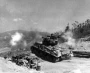 A US Medium Tank M4A3E8  tank fires from a prepared position during the Korean war