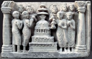 Lay devotee couple in Hellenistic dress (right, man holding a lamp), and Buddhist monks (shaven, left), circambulating a stupa.