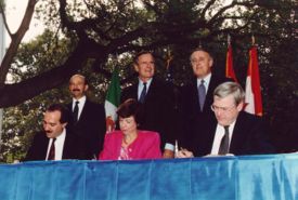 NAFTA Initialing Ceremony, October 1992.  From left to right: (standing) President Carlos Salinas, President Bush, Prime Minister Brian Mulroney; (seated) Jaime Serra Puche, Carla Hills, Michael Wilson.