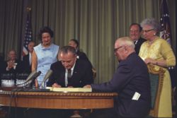 Truman (seated right) and his wife Bess (behind him) attend the signing of the Medicare Bill on July 30, 1965, by President Lyndon Johnson.