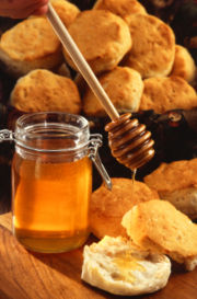 A jar of honey, shown with a wooden honey server and scones.
