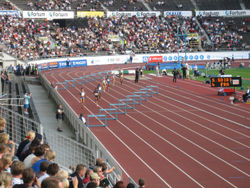 A women's 400 metre hurdles race on a typical outdoor red rubber track.