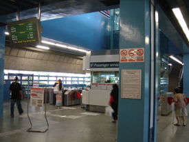 Concourse level of Queenstown MRT Station, showing a plasma display screen, passenger service centre and faregates.