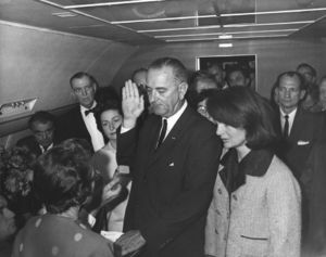 Lyndon B. Johnson being sworn in aboard Air Force One by Federal Judge Sarah T. Hughes, following the assassination of John F. Kennedy. Alongside Johnson is Jacqueline Kennedy, wife of slain President John F. Kennedy.